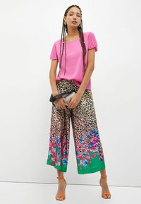 Top corto a maniche corte plissettato rosa abbinato a pantaloni larghi con stampa leopardata, caratterizzati da accenti floreali in blu e rosa, completati con un orlo verde.