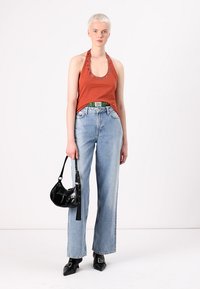 Haut-halter couleur rouille avec un col clouté, jeans bleu clair à jambes larges, sac à main noir en verni et escarpins noirs à bout pointu.