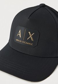 Čierna baseballová čiapka s zlatou nášivkou "A|X Armani Exchange" na prednej strane, s prešitým zakriveným krempou a vrchným gombíkom.