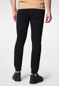 Czarne dresy wykonane z miękkiego materiału, z tapered legs, elastycznymi mankietami i tylną kieszenią. W połączeniu z czarnymi trampkami.