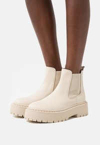 Bottines en cuir beige avec des panneaux latéraux élastiques, semelle plateforme épaisse et couture texturée. Design minimaliste pour un usage décontracté.