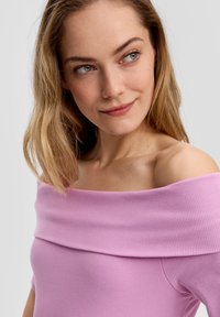 Blúzka bez ramienok v svetloružovej rebrovanej látke, s širokým výstrihom a priliehavým strihom, ktorý zdôrazňuje hladkú textúru.