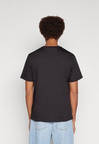 Czarny T-shirt z krótkim rękawem i okrągłym dekoltem. Wykonany z gładkiego, lekkiego materiału i o luźnym kroju, przedstawiony z widoku z tyłu.