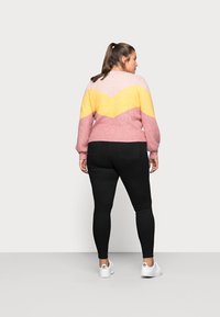Pastel-colored sweater with a chevron pattern in pink, yellow, and cream, paired with black leggings and white sneakers.