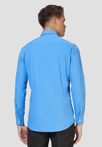 Camicia a maniche lunghe azzurra chiara realizzata in tessuto morbido, con colletto classico, polsini con bottoni e orlo curvo.
