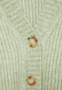Tissu en maille côtelée vert clair avec deux grands boutons ronds beiges sur la fermeture d'un cardigan à col en V.