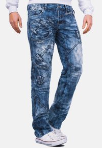 Jeans in denim in tonalità di blu chiaro e scuro con un finish sbiadito, caratterizzati da motivi di cucitura unici, numerose tasche e accenti in metallo.