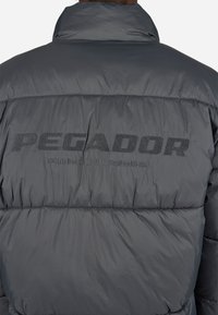 Graue Pufferjacke mit hohem Kragen, mit "PEGADOR" auf dem Rücken bestickt. Hergestellt aus einem glatten, isolierten Material mit einem gesteppten Design.