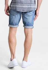 Vaaleansiniset denim-shortsit, joissa on käännetyt lahkeet. Varustettu takataskuilla ja sileällä pinnalla, käytetään valkoisten tennareiden kanssa.