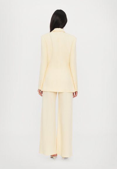 Light yellow tailored suit featuring a long blazer and wide-leg trousers; smooth fabric with subtle texture and three button accents on sleeves.