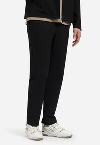 Zwarte, taps toelopende broek met een soepele textuur en zijnaad, gecombineerd met witte sneakers met grijze accenten en veters.