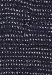 Tessuto blu navy con un motivo testurizzato di piccole macchie bianche e linee. Include una piccola tasca a toppa con un bordo a contrasto nella parte superiore.