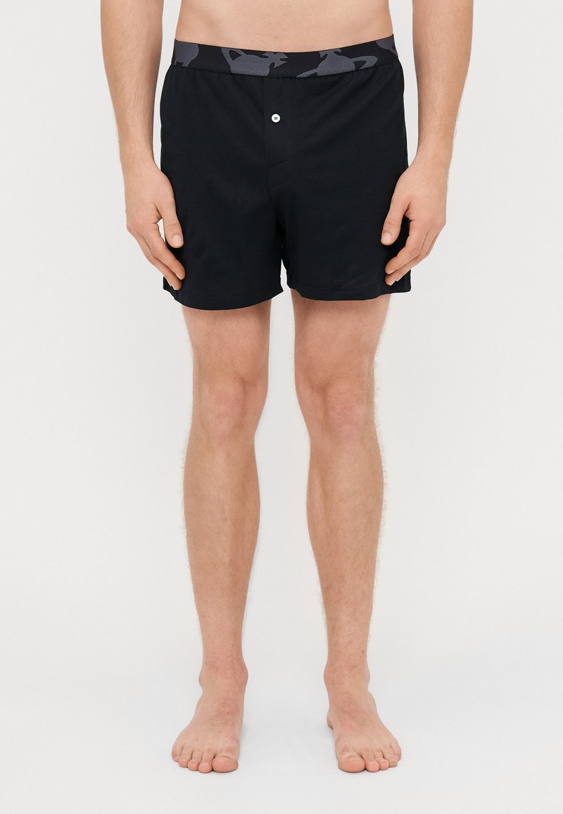 Schwarze Badehorts mit einem gemusterten elastischen Bund, ausgestattet mit einem Knopfverschluss vorne und einem klassischen Schnitt, hergestellt aus leichtem Material.