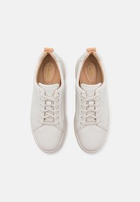 Baskets en cuir blanc avec une texture lisse, un design à lacets et un accent beige au niveau du talon. L'intérieur possède une semelle intérieure de couleur claire.