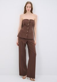 Top marrone senza spalline con bottoni dorati, vestibilità sartoriale e due tasche frontali abbinato a pantaloni larghi coordinati e sandali con tacco.