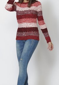 Czerwono-biały sweter w paski wykonany na drutach z długimi rękawami; teksturowany materiał; zestawiony z niebieskimi dżinsami z przetarciami.
