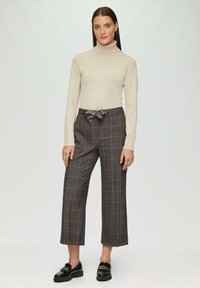 Beżowy sweter z golfem zestawiony z szarymi spodniami w kratę, z kokardką w talii i czarnymi loafersami. Miękka dzianina i strukturalny materiał.