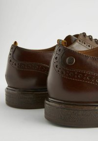 Braune Lederschuhe mit Broguemuster, runder Zehe und strukturiertem Gummisohle. Enthält eine kleine Schlaufe und einen Metallelement.