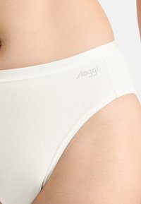 White cotton bikini brief with a soft texture, featuring a wide waistband and a subtle logo on the side. Seamless design for comfort.