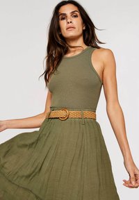 Top verde de canalé combinado con una falda texturizada de oliva, ceñida con un cinturón trenzado de color marrón claro que presenta una hebilla redonda. La tela suave cae con elegancia.