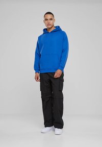 Sudadera azul con un bolsillo tipo canguro y cordones, combinada con pantalones cargo negros que tienen bolsillos laterales, y zapatillas blancas.