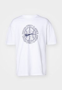 Witte T-shirt met zwart cirkelvormig grafisch motief van een kettingscherm en kettingen, met een Nike swoosh en de tekst "Swoosh Street Classics" herhaald eromheen.
