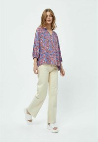 Blusa leggera viola con motivo paisley, scollo a v e maniche a tre quarti. Abbinata a pantaloni larghi color crema e sandali con zeppa bianchi.
