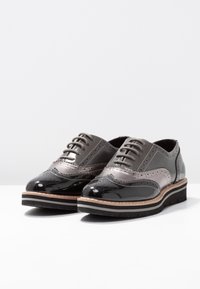 Chaussures Oxford en cuir présentant un design bicolore gris et noir, des détails brogués, une fermeture à lacets plate et une semelle superposée.
