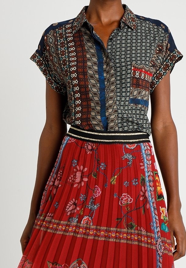 Chemise à manches courtes à motifs avec des accents bleus et une poche plaquée, associée à une jupe plissée rouge ornée de broderies florales et colorées.