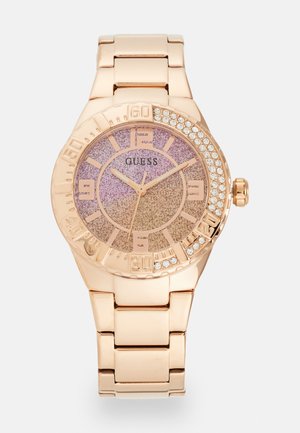 Orologio color oro rosa con un quadrante gradiente rosa glitterato, contrassegnato da grandi numeri e accentuato da una lunetta di strass. Cinturino a bracciale in metallo.