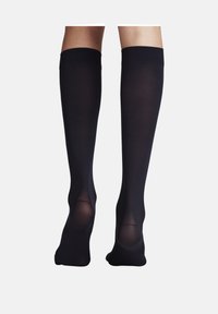Calzini neri alti fino al ginocchio con una texture liscia e sezioni trasparenti nella zona del piede. Banda superiore a coste per una vestibilità sicura e una sottile lucentezza.