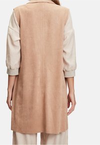 Zamszowa kamizelka w kolorze jasnobrązowym o prostym kroju, bez zapięć i z kołnierzem z klapami. Charakteryzuje się miękką fakturą i podwiniętymi rękawami z jasnoszarym akcentem.