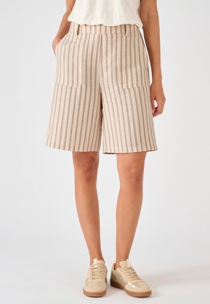 Beige knielange shorts met verticale bruine strepen, voorzakken, gedragen met beige sneakers en een wit ingestopt topje.