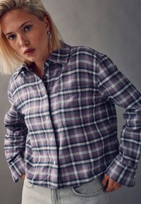 Plaid shirt in purple, gray, and black with a button-up front and long sleeves. Textured fabric shown with relaxed fit and small chest pocket.