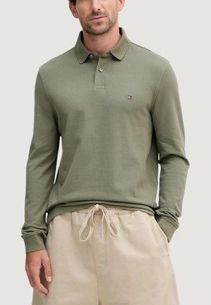 Polo a maniche lunghe in cotone verde oliva. Presenta un colletto piatto, una patta con bottoni e un piccolo logo sul petto. Abbinata a pantaloncini beige con coulisse.