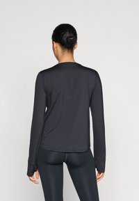 Μαύρη αθλητική μπλούζα με μακριά μανίκια, στρογγυλή λαιμόκοψη, λεία υφή και θήκες για τους αντίχειρες στους μανικιού, συνδυασμένη με εφαρμοστά μαύρα κολάν.