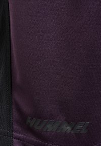 Paarse sportshorts met een gestructureerde afwerking, met zwarte accenten en het "HUMMEL" logo in het zwart op de onderste sectie.