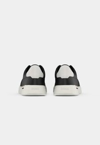 Paire de baskets noires et blanches vues de dos avec le mot « BOSS » embossé sur les semelles blanches.