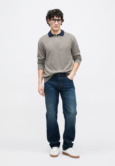 Helehall hall kampsun tumesinise kraega, sinised teksapüksid ja valged tennised. Materjal näib pehme, lõdvestunud istuvusega ja detailse õmblemisega.