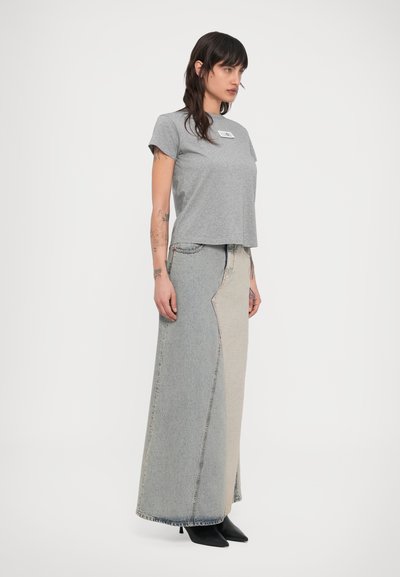 Grå T-skjorte med en logopatch, kombinert med et langt, tofarget denimskjørt med kontrasterende lyse og mørke seksjoner, og svarte hæler.
