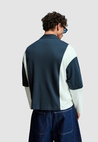 Tröja med krage, med en färgblockerad design i mörkblått, krämfärgat och ljust grått. Slät tygkvalitet och lös passform.