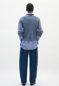 Modra volnena pulover s zavitimi manšetami preko modre in bele črtaste srajce, v kombinaciji z širokimi modrimi kavbojkami. Enostaven, sproščen kroj.