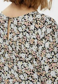 Blommig blus med svart bakgrund och mönster av vita och pastellfärgade blommor, nyckelhålsdetalj i ryggen och lättviktig tyg.