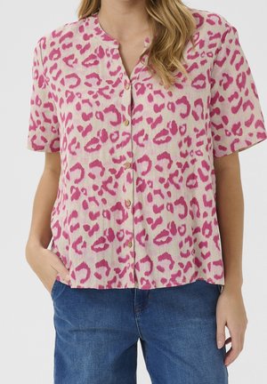 Korte mouwen blouse van licht materiaal met een roze luipaardpatroon, voorzien van een V-hals en knoopsluiting. Model draagt blauwe jeans.
