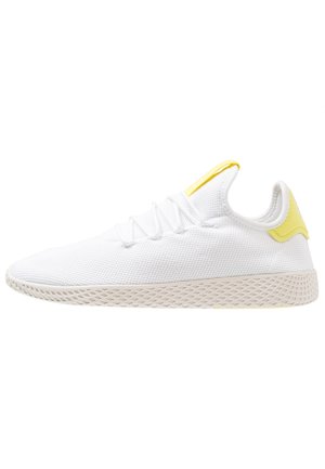Hvid mesh-sneaker med beige tekstureret sål, hvide snørebånd og gule accenter på hæl og tunge mod hvid baggrund.