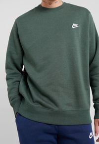 Grön Nike sweatshirt med rund halsringning och ribbad mudd. Har en liten vit logotyp på vänster bröst. Mjuk, texturerad tyg.