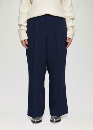Marineblauwe wijde broek met dubbele plooien, gemaakt van een soepele stof. Gecombineerd met een crèmekleurige trui en zilveren schoenen.
