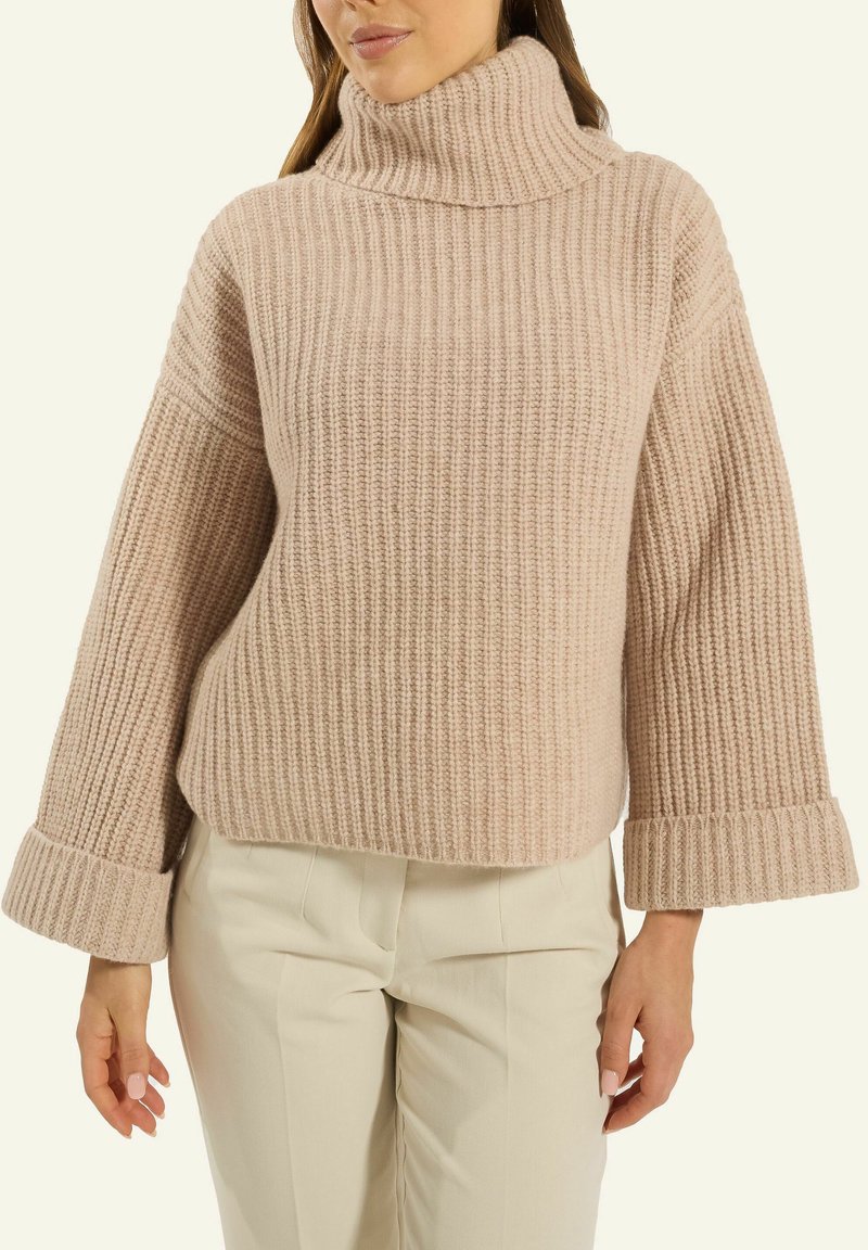 Helle rosa gerippte Strickjacke mit hohem Kragen und breiten Bündchen, im entspannten Schnitt und mit strukturiertem Muster. Kombiniert mit cremefarbenen Hosen.