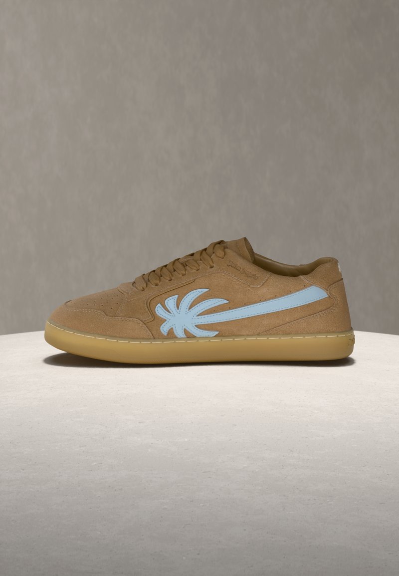 Καφέ σουέντ αθλητικό παπούτσι με φ ωτεινό γαλάζιο λογότυπο φοίνικα στο πλάι και σοκολατί σόλα, εκτεθειμένο σε μια λεία γκρίζα επιφάνεια με γκρίζο φόντο.