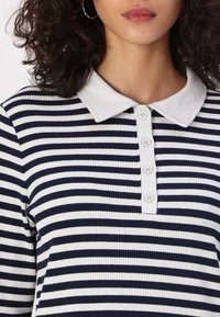 Marine- og hvitstripet polo-skjorte med ribbestruktur, med en myk krage og fem knapper foran.